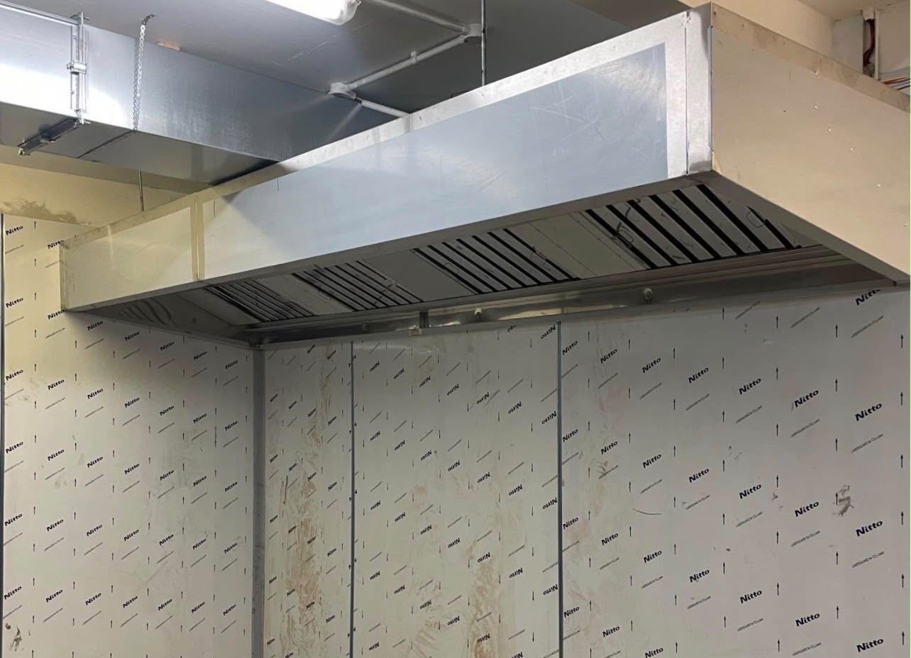 Stainless steel extraction canopy above a stainless splashback wall in a commercial kitchen